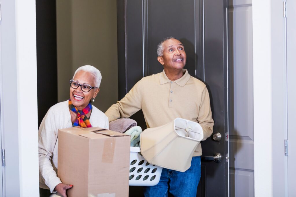 An older couple joyfully carrying boxes into their new home