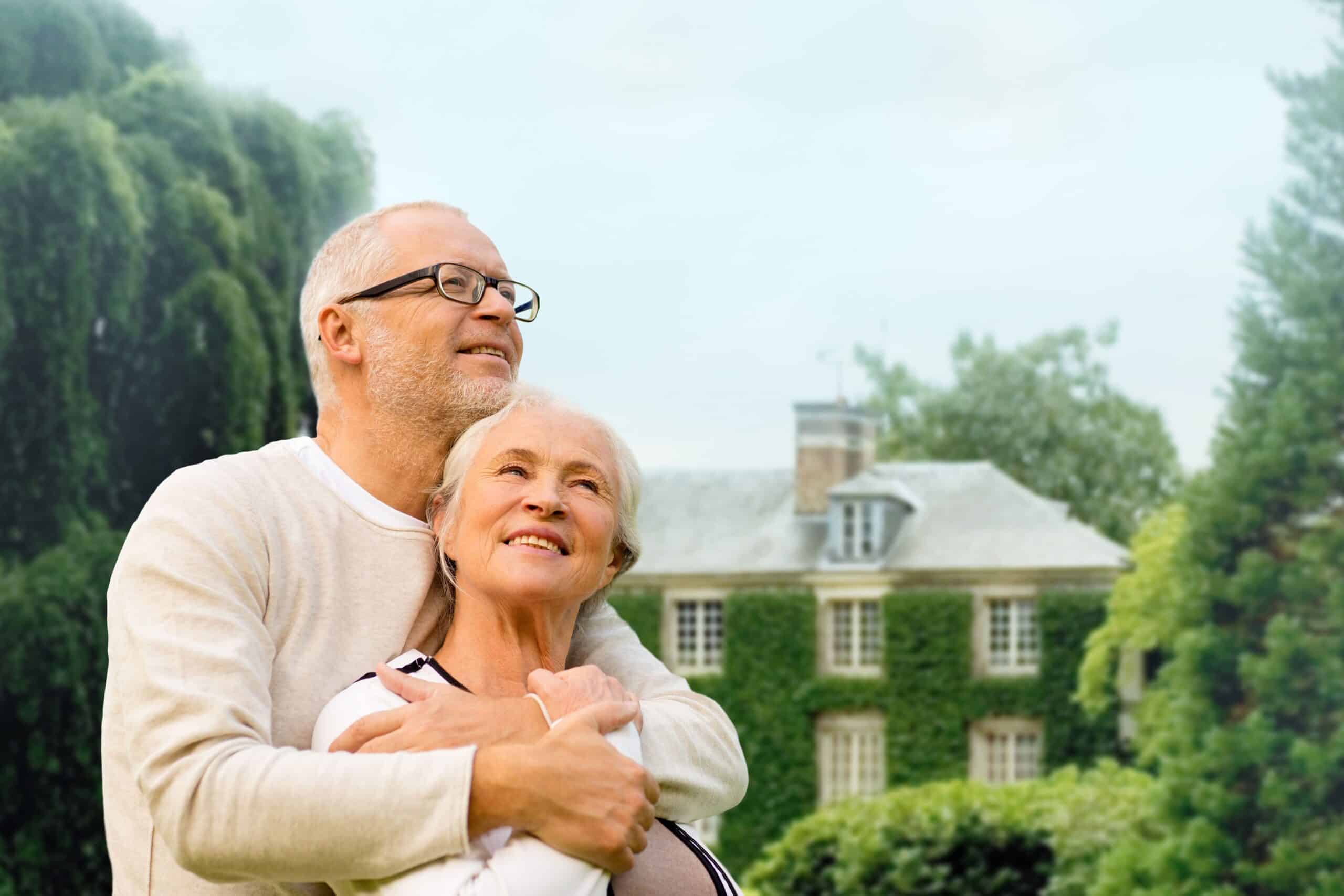 An older couple joyfully embracing in front of their charming home